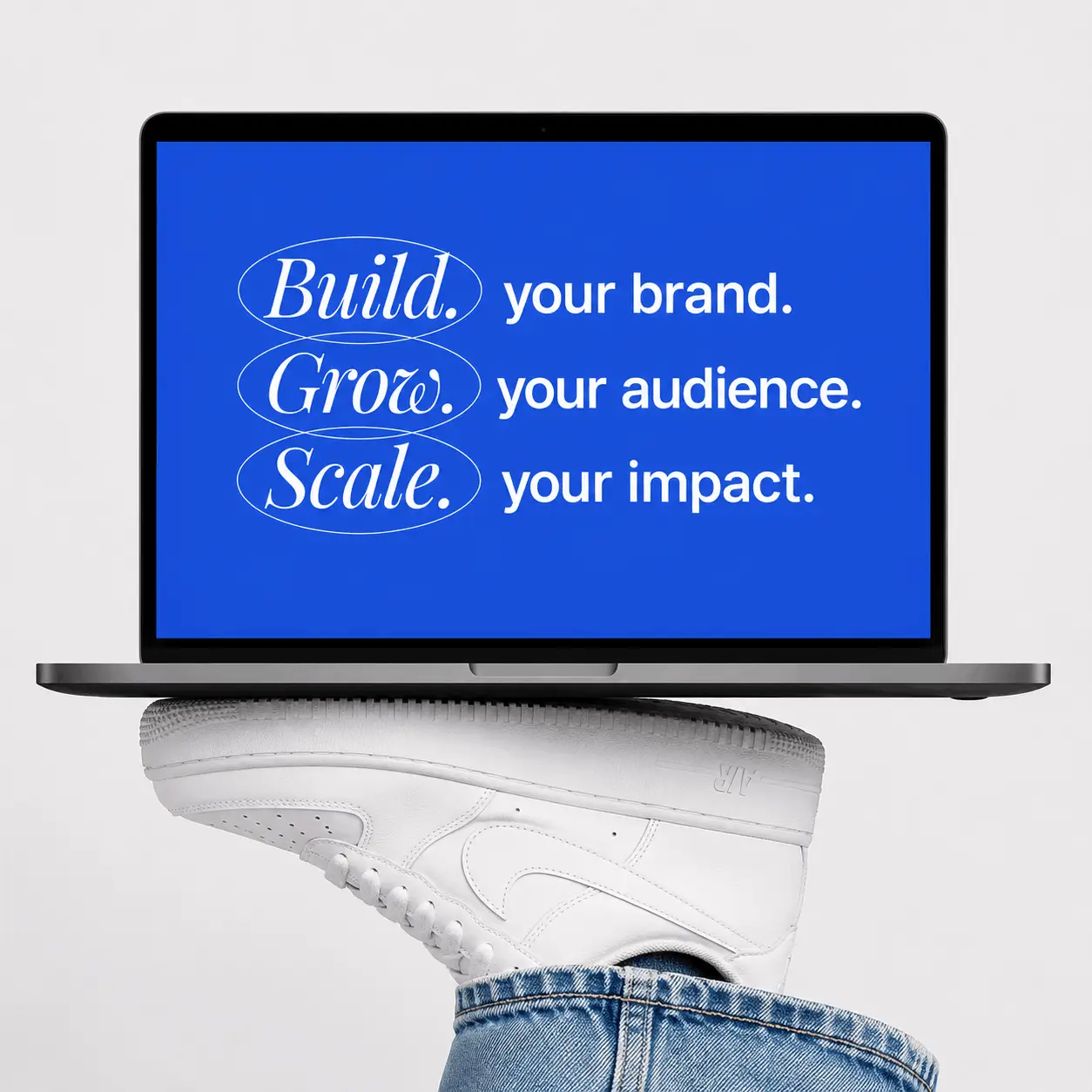 An open laptop balanced on top of a white Nike sneaker. The bright blue screen displays white text that reads: Build your brand. Grow your audience. Scale your impact